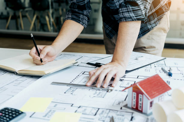 istock Interior designer or architect reviewing blueprints and holding pencil drawing on desk at home office. 1645596082