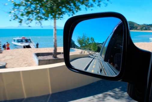 Looking at the view from a car mirror. The scenery surrounding is Kaiteriteri Beach in the Abel Tasman National Park, New Zealand in blur. Selective focus is on the view in the reflection.