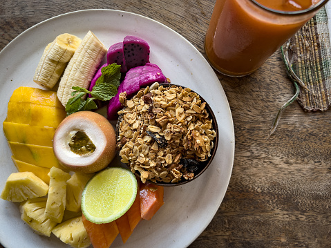 Healthy vegan breakfast of granola, papaya, pineapple, mango, banana, dragon fruit and guava with a carrot and fruit smoothie.  Served in a cafe in Ubud, Bali, Indonesia