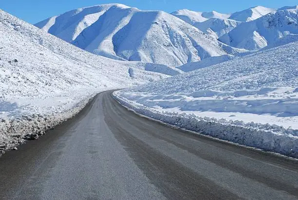 A road, the Great Alpine Highway, leads through the snow into the beginning of the Southern Alps, New Zealand.