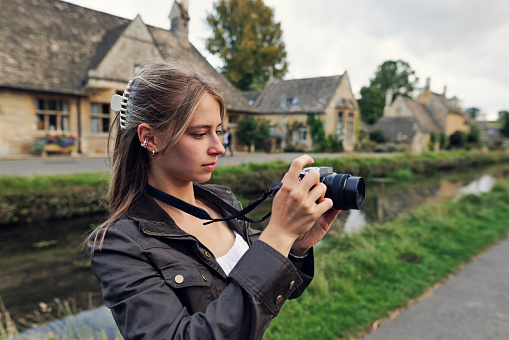 Teenage girl enjoying summer vacations in Gloucestershire, United Kingdom. 
The girl is walking in the beautiful village of Lower Slaughter. The River Eye is flowing in the center of the village.
Shot with Canon R5