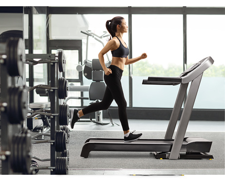 Full length profile shot of a young female in black leggings running on a treadmill at a gym