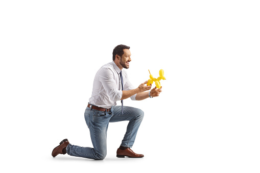 Profile shot of a man kneeling and holding a dog made from a balloon isolated on white background