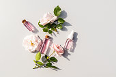 Several different glass cosmetic bottles with serum with bud flower rose extract and rose water for facial skin care. The top view is flat styling