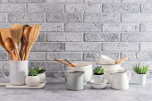 A set of various kitchen utensils on a stone countertop opposite a gray brick wall. front view. modern kitchen space.