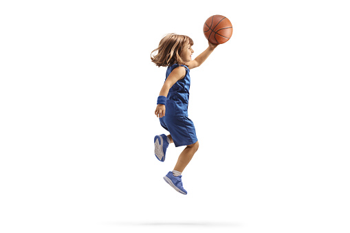 Girl in a blue sports jersey holding a basketball and jumping isolated on white background