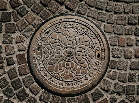 Manhole cover in cobblestoned pavement in Budapest, Hungary 11. August 2023.