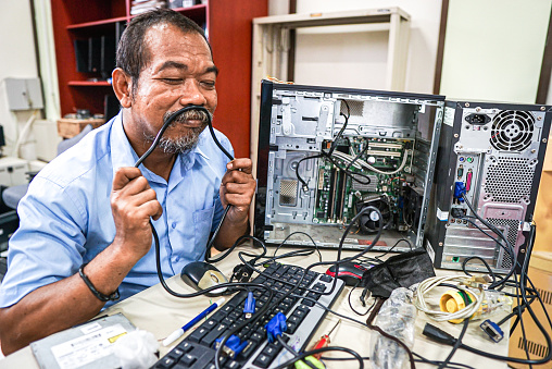Funny looking man holding a black wire is trying to fix his computer. Engineer posing with computer components .