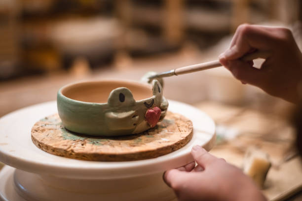 girl hands, pottery studio and painting cup in workshop for makes a creative mug in the form of a frog. Painter, ceramics product and brush process, artistic pattern or production in small business