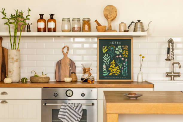 istock Creative composition of kitchen interior with mock up poster frame, silver oven, tap, stylish cup, jar with spices, brown bottle, white wall, tiles and personal accessories. Home decor. Template. 1645858440