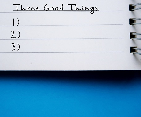Notebook on blue copy space background with handwritten text Three good things - gratitude practice journal to track daily reflections, find three good things to be grateful for