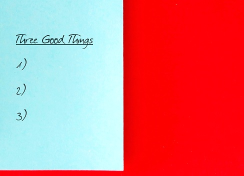 blue paper on red copy space background with handwritten text Three good things - gratitude practice journal to track daily reflections, find three good things to be grateful for