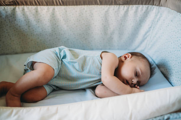 a little baby is sleeping in his crib next to the parents' bed - thumb sucking cute small lying down imagens e fotografias de stock