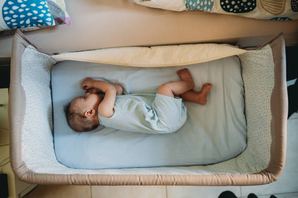 小さな赤ちゃんが両親のベッドの隣のベビーベッドで寝ています - finger in mouth 写真 ストックフォトと画像