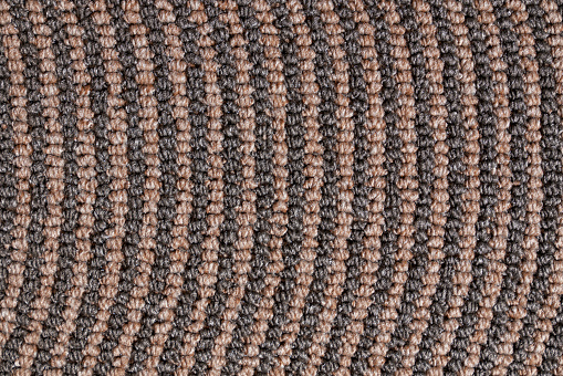 Dark relief texture of rolled up carpet edge for unusual background. Close up of brown pattern of synthetic tight knitted jute rows. Concept of textures and background.