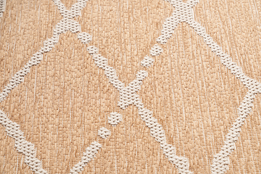 Texture of decorative pattern carpet fabric for background. Close up of beige lint-free cotton rug, with geometric knitted vertical rhombus ornament. Concept of backgrounds and textures.