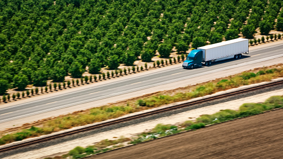 Aerial view of articulated lorry driving on major road amidst railway track and vineyard, California, USA.