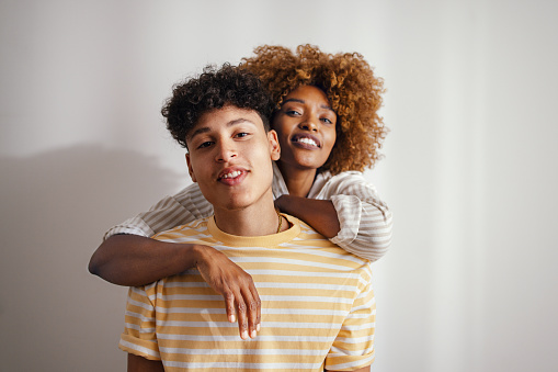 Portrait of a beautiful African American woman with her handsome teenage son. She is standing behind him, hugging him. They are both smiling and looking at the camera.