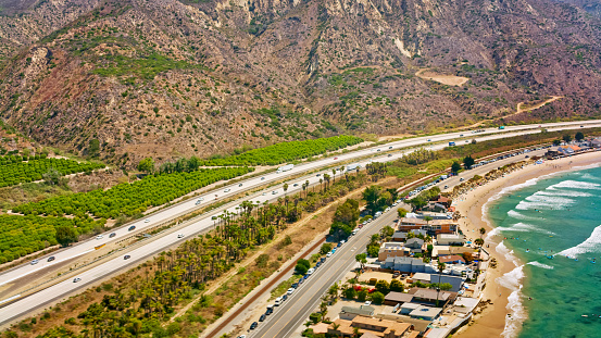 Aerial view of vehicles driving on coastal road by vine yards along coastline, California, USA.