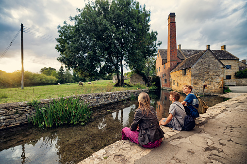 Three teenage kids enjoying summer vacations in Gloucestershire, United Kingdom. 
They are sightseeing the beautiful village of Lower Slaughter. Kids are looking at the beautiful view of the old mill.
Shot with Canon R5