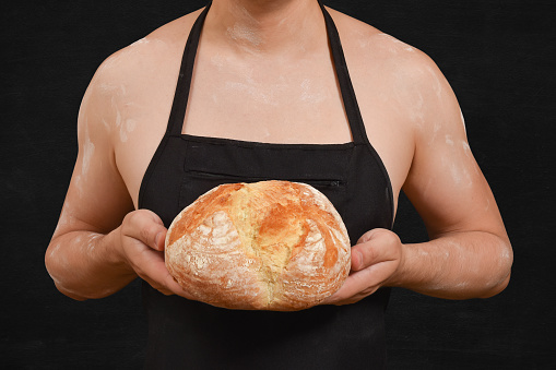 Male baker holding freshly baked bread in his hands on a black background. Cooking concept