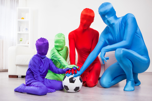 Colorful family in zentai suits joining hands on a soccer ball. Family is presented in different colors as unrecognizable people due to stop racism concept in mind. Idea in this series of photo was to simply show people as people without characteristics they can be defended as good or bad, black or yellow or white … So STOP RACISM
