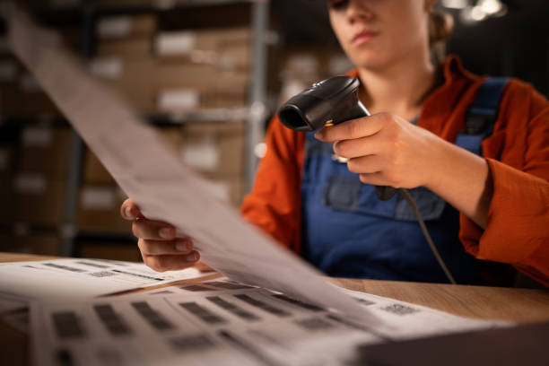 Close up of warehouse worker scanning barcodes on paper working in a large warehouse, sitting at table Close up of warehouse worker scanning barcodes on paper working in a large warehouse, sitting at table. Copy space traceability stock pictures, royalty-free photos & images