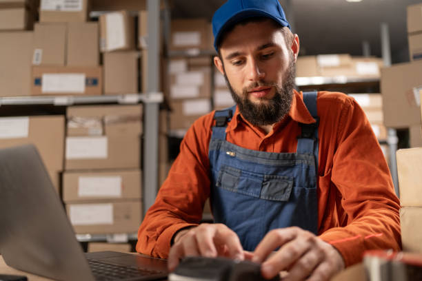 istock Young man working in Warehouse retail center with cardboard boxes, e-commerce online orders, using laptop computer and pos-terminal for payment 1646034421