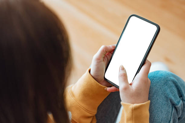 istock Hand of woman touching mockup blank screen mobile smartphone on sofa at home, White empty space for advertise text. 1646044557