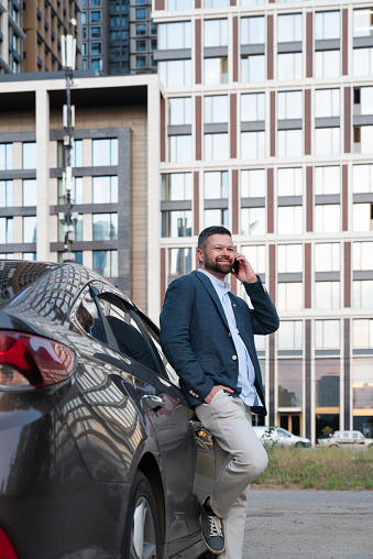 Businessman talking on the phone near the car on the background of a skyscraper