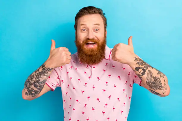 Photo of impressed overjoyed man with redhair beard wear pink t-shirt show thumb up good job staring isolated on blue color background.