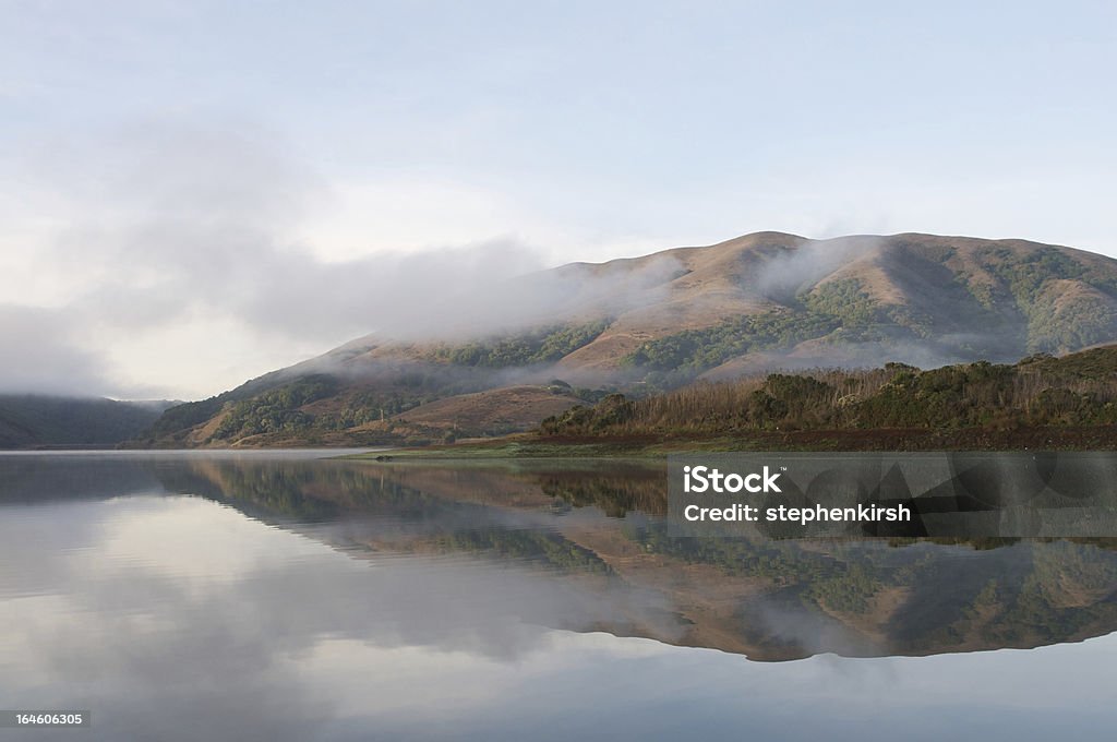 Hills reflected in surface of lake on a foggy morning Beauty In Nature Stock Photo