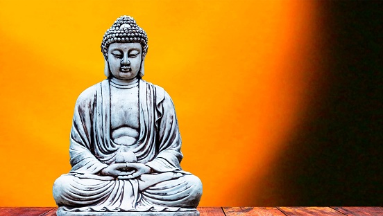 A closeup of a Buddha statue in a meditative pose, illuminated by a golden background.