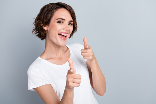 Photo of pretty excited woman dressed white t-shirt showing fingers you empty space isolated grey color background.