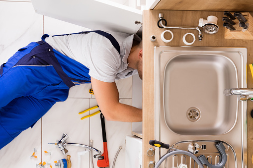 High Angle View Of Male Plumber In Overall Fixing Sink Pipe