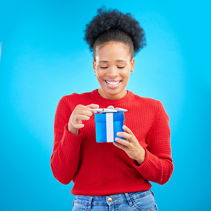 Smile, birthday and a black woman with a gift on a blue background for happiness or a surprise. Holding, box and a young African girl with a present for a celebration isolated on a studio backdrop