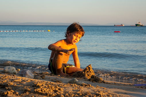 Beautiful boy playing in the sand by the sea. In the evening sun, he plays different creative games with the sand and the sea.