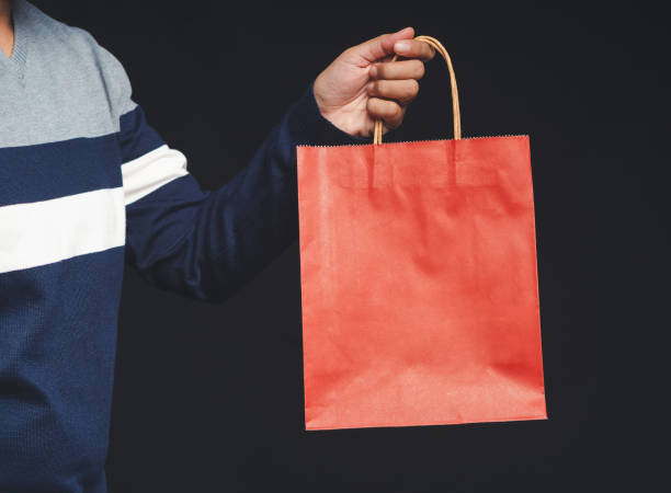 istock Hand holding a red paper bag with a handle on a black background 1646237954
