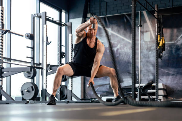 istock Athletic young man with battle rope doing exercise in functional training fitness gym. 1646244641