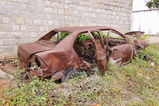 Mysuru, Karnataka, India-July 5 2023; A Moving picture of an Isolated Sedan Car totally rusted and junked after a collision, lies amidst the plants and shrubs in India.