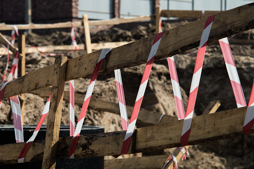 Wooden railing with a ribbon in red and white colors. Photo of road repairs with blurred background.