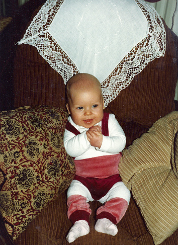 Baby sitinig and holding a comb with two hands. Looking directly into camera. Black and white photo. Retro style.