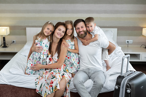 Young family: parents with children sit on the bed in the hotel and laugh. Traveling with children