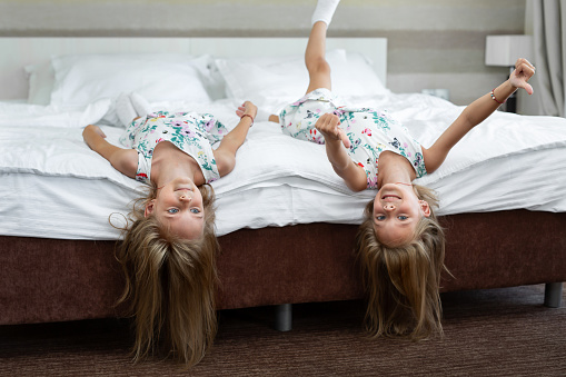 Two twin sisters are lying on the bed upside down.