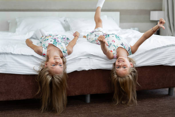 duas irmãs gêmeas estão deitadas na cama de cabeça para baixo - multiple birth - fotografias e filmes do acervo