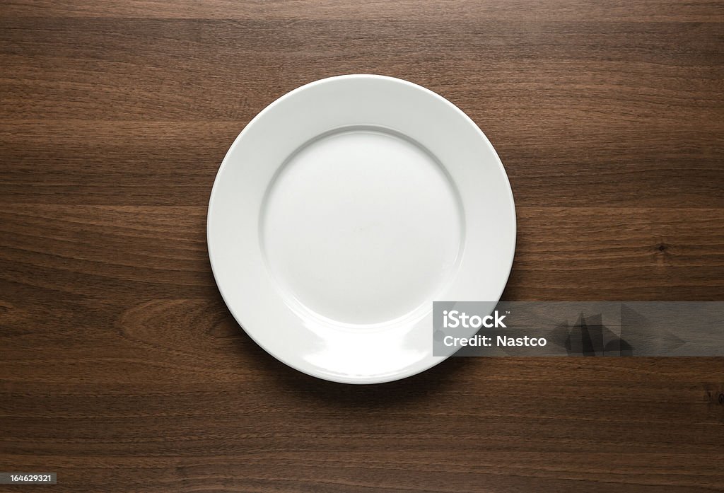 White empty plate at the table Close up of white empty plate at the wooden table with copy space High Angle View Stock Photo