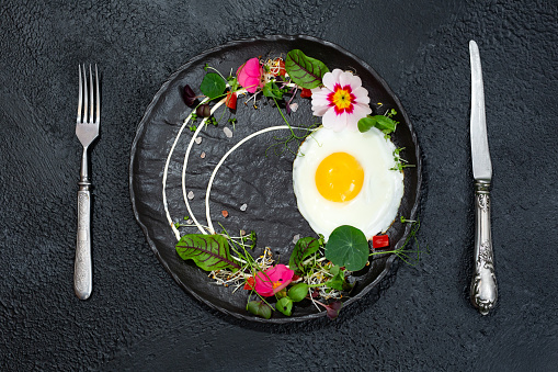 Fried egg with a decor of microgreens, food flowers, sorrel and nasturtium.