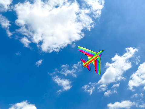 Multicolored kite flies in the blue sky on a sunny day. Empty space for an inscription. Multicolored kite in the form of an airplane. High quality photo