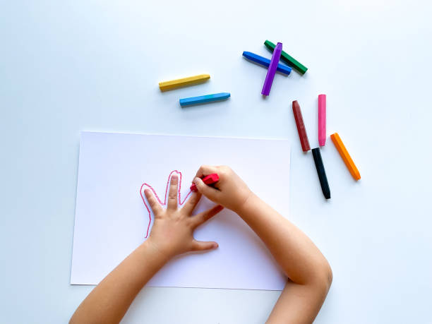 istock Childrens hands draw their hand with wax crayons on white paper, top view. 1646321964