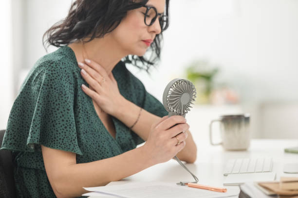donna matura che soffre di vampate di calore in ufficio - menopause foto e immagini stock